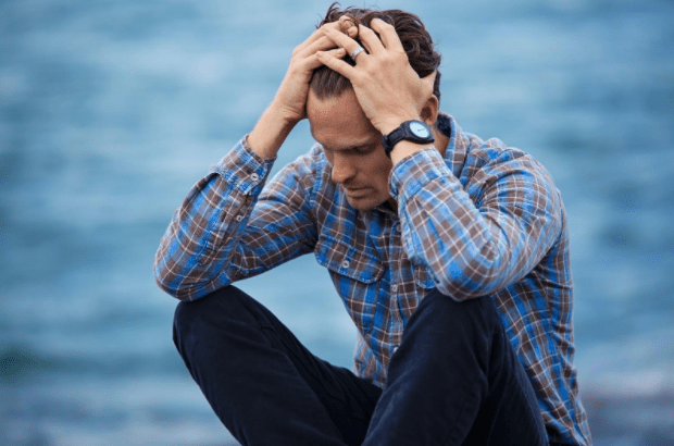 Man with hands on head near ocean